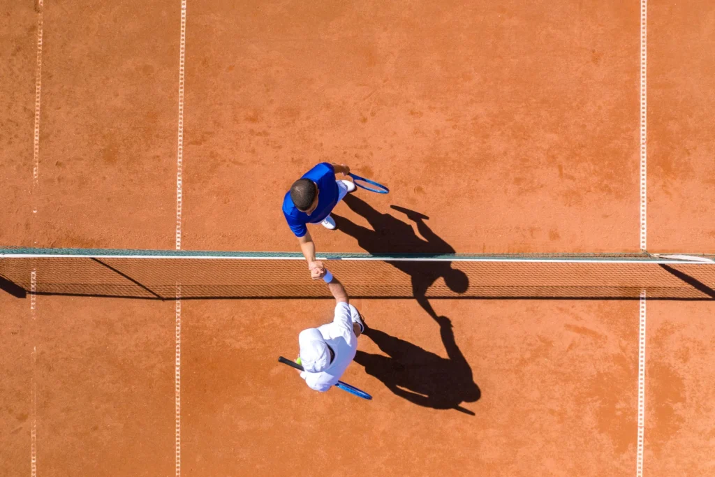 Två tennisspelare som tar varandra i hand över nätet – bild som illustrerar paralleller mellan tennis och förhandling.