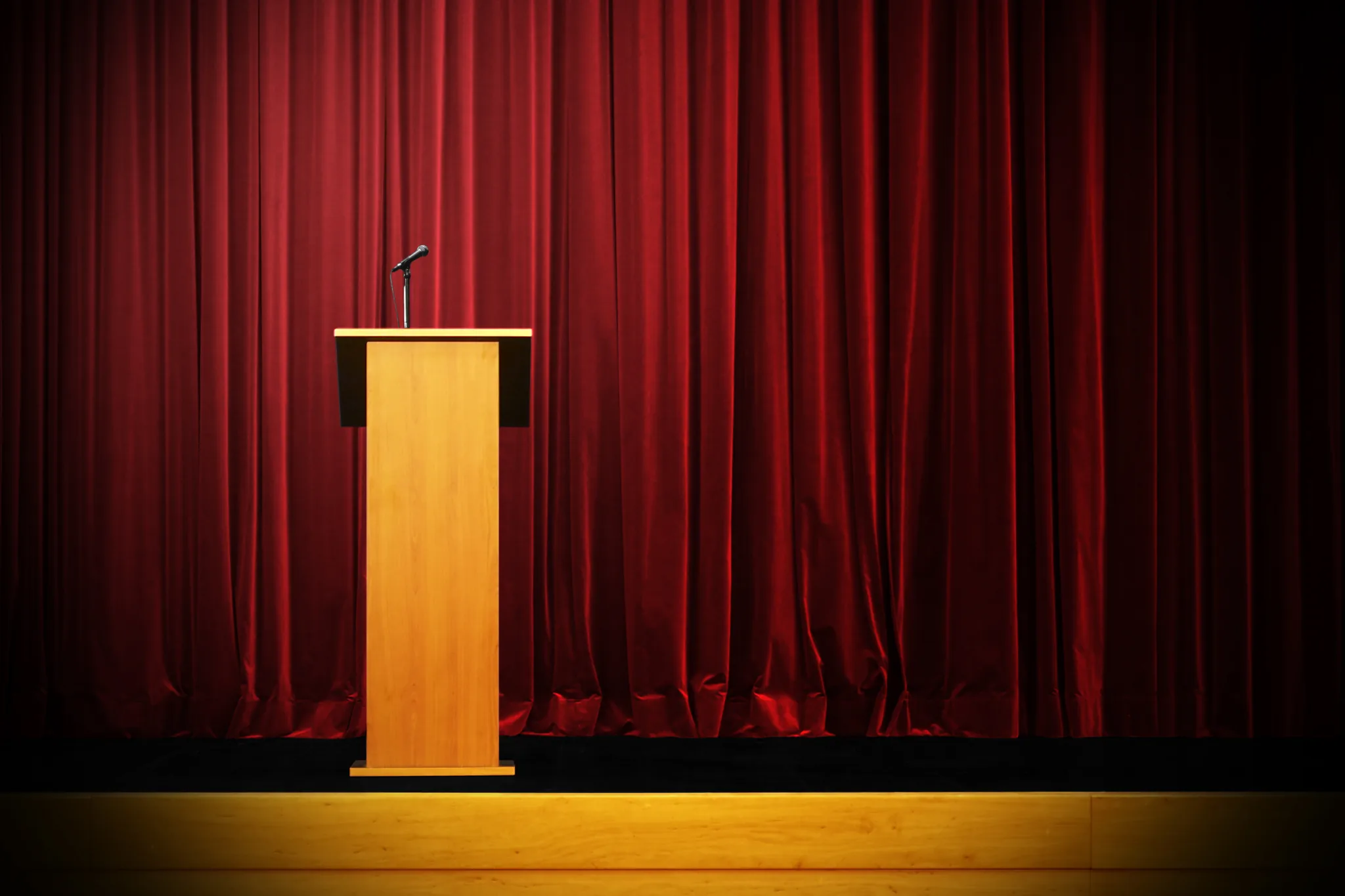 Podium med mikrofon framför scenridå – symbol för retorik, public speaking och
presentationsteknik.