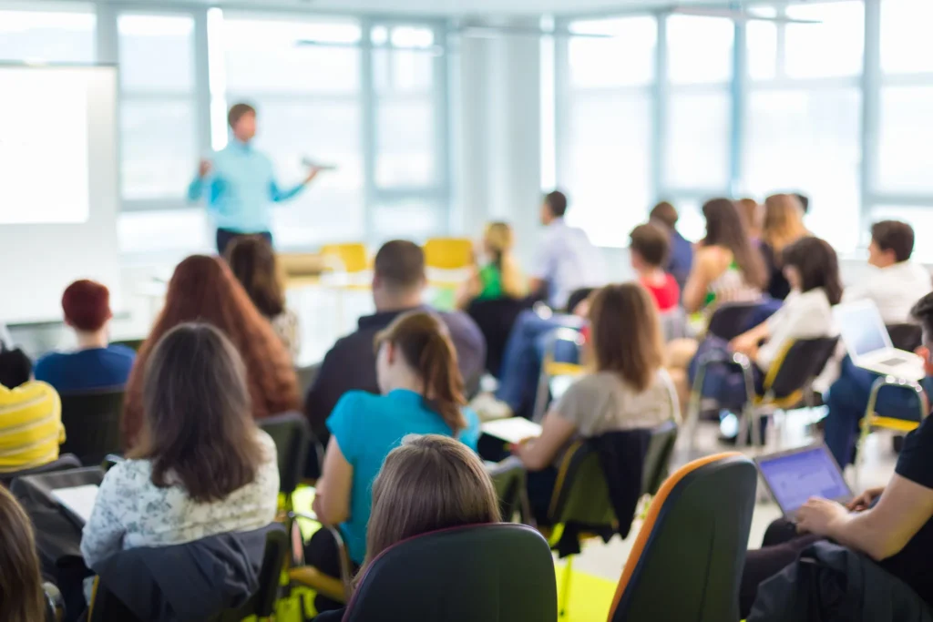 Föreläsare som håller utbildning och workshop inför publik i modern konferensmiljö.